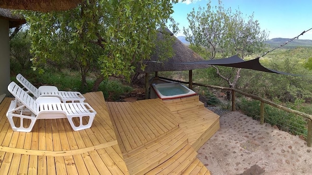 Une terrasse en bois avec deux chaises longues blanches et un jacuzzi.
