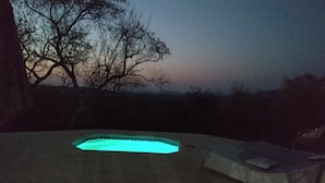 Une piscine dont le bord est illuminé, entourée d ’un espace abrité avec un banc.