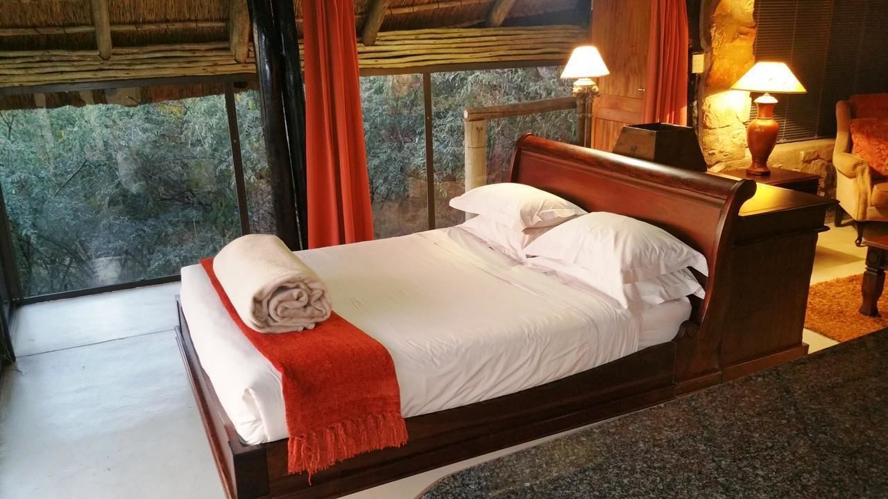 Ein Bett mit weißer Bettdecke und roter Decke, ein hölzernes Kopfstück und zwei Nachttischlampen.