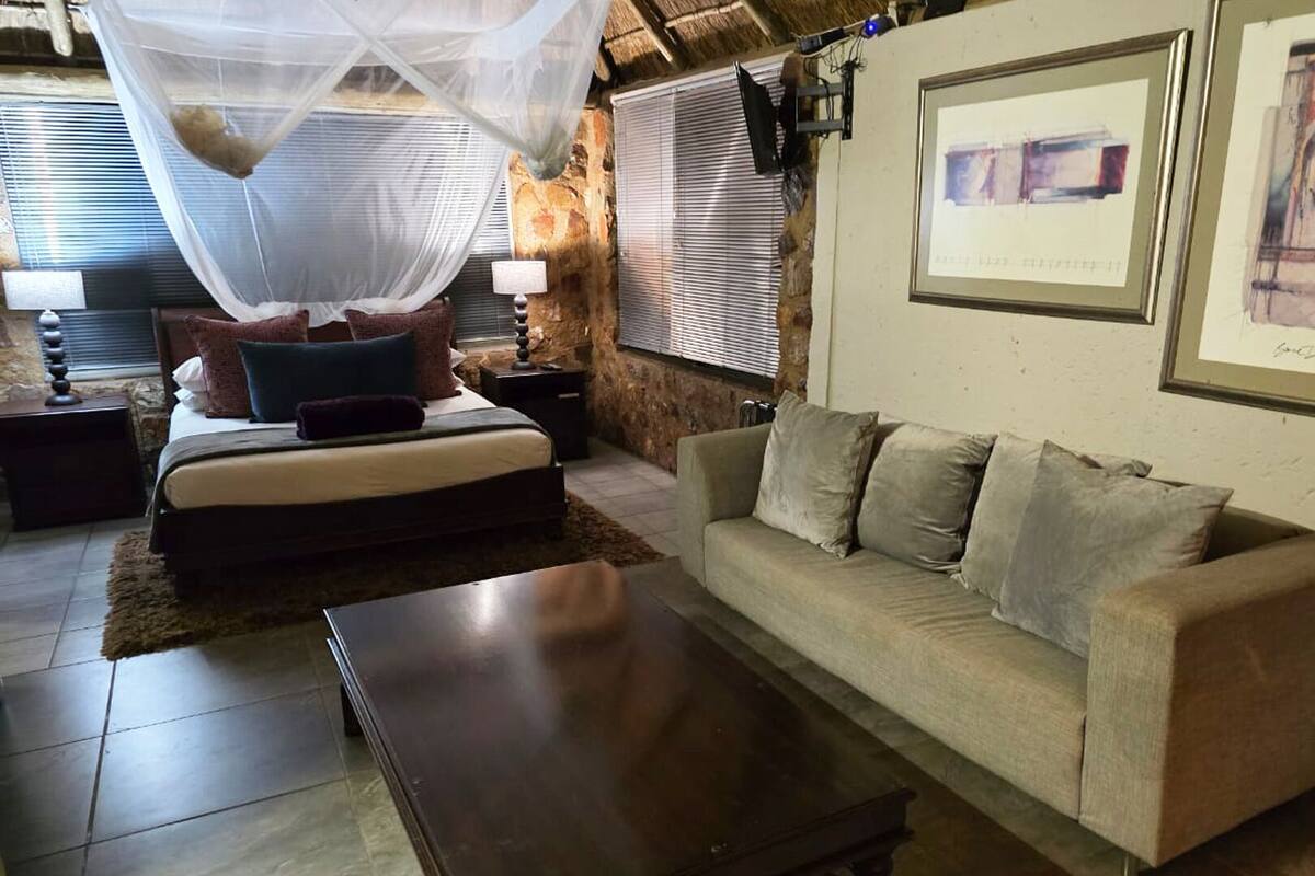 A bedroom with a bed, a nightstand, a bedside table, a sofa, and a wall-mounted TV.