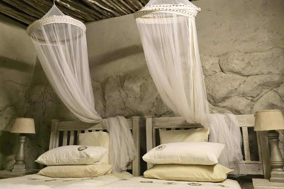 A bedroom with a stone wall, two wooden beds with white bedding, and a canopy bed with white drapes.