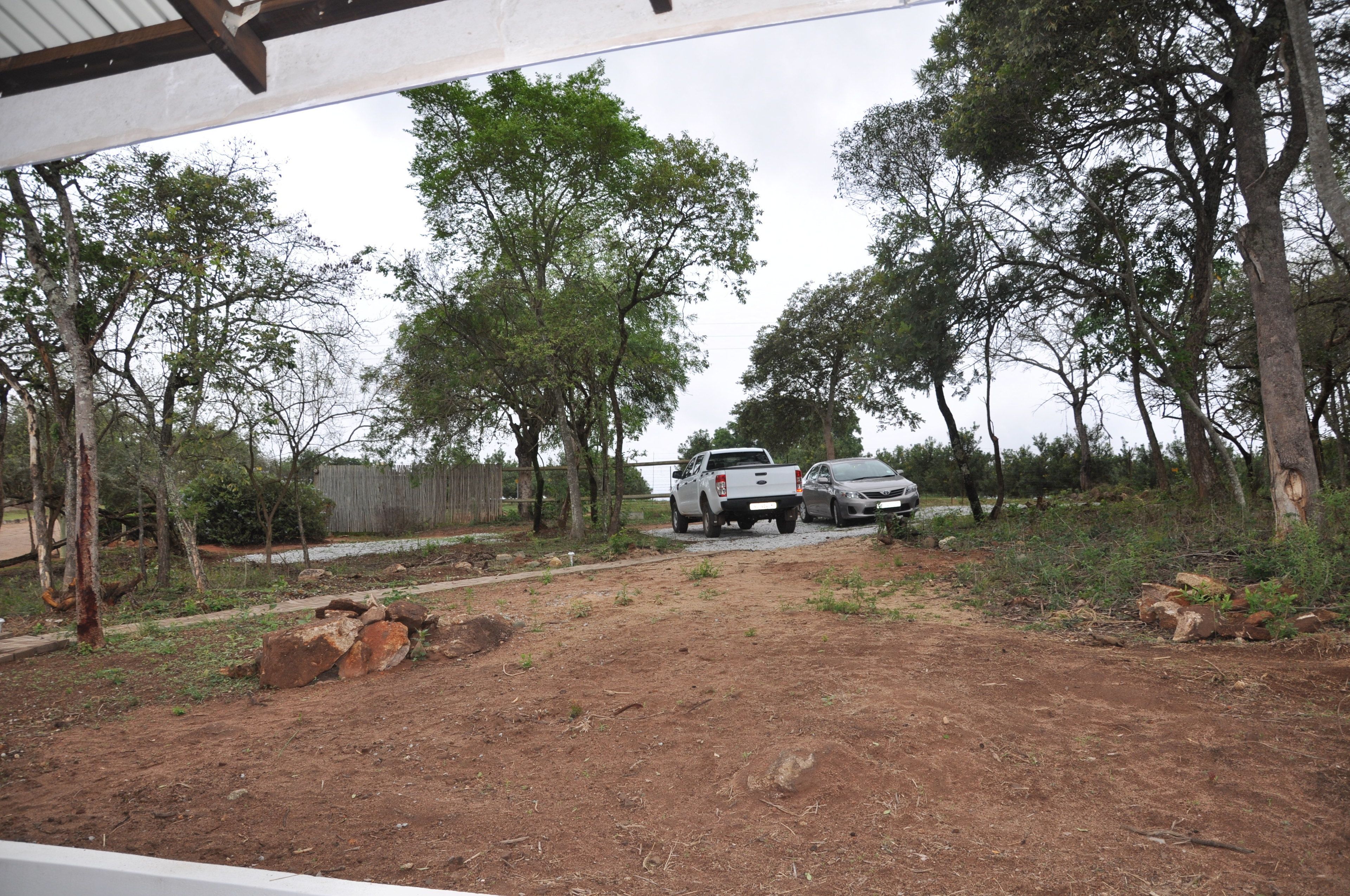 A dirt path leading to a white pickup truck parked near a fence with trees on either side.