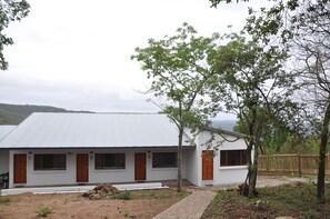 Simple, single-story building surrounded by a natural landscape with trees and a fence.