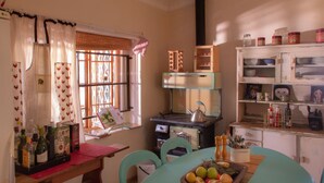 Une cuisine avec un four ancien, un panier de fruits sur la table et divers ustensiles de cuisine rangés sur des étagères.