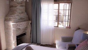 Une chambre à coucher avec une cheminée, un lit, une chaise et une fenêtre avec des rideaux.