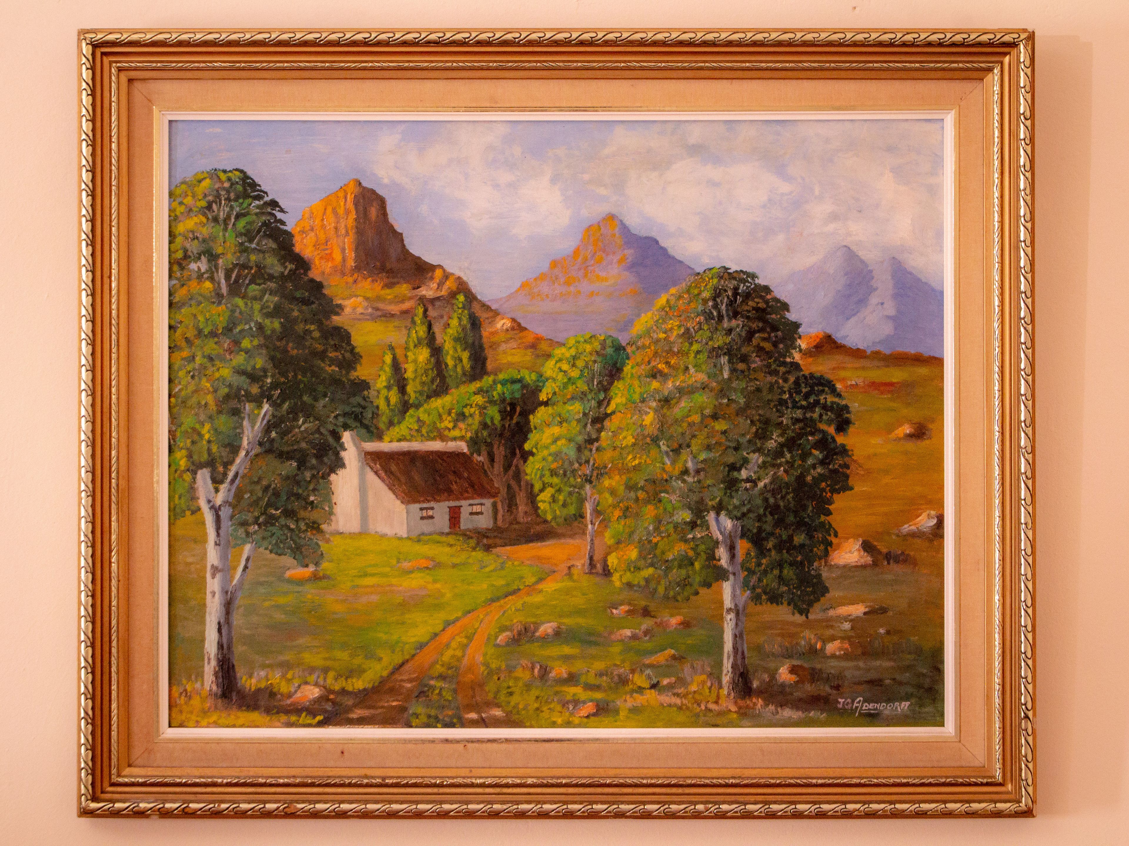 A framed painting of a rural landscape with a house, trees, and mountains.