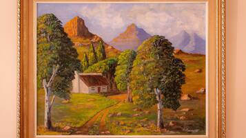 A framed painting of a rural landscape with a house, trees, and mountains.