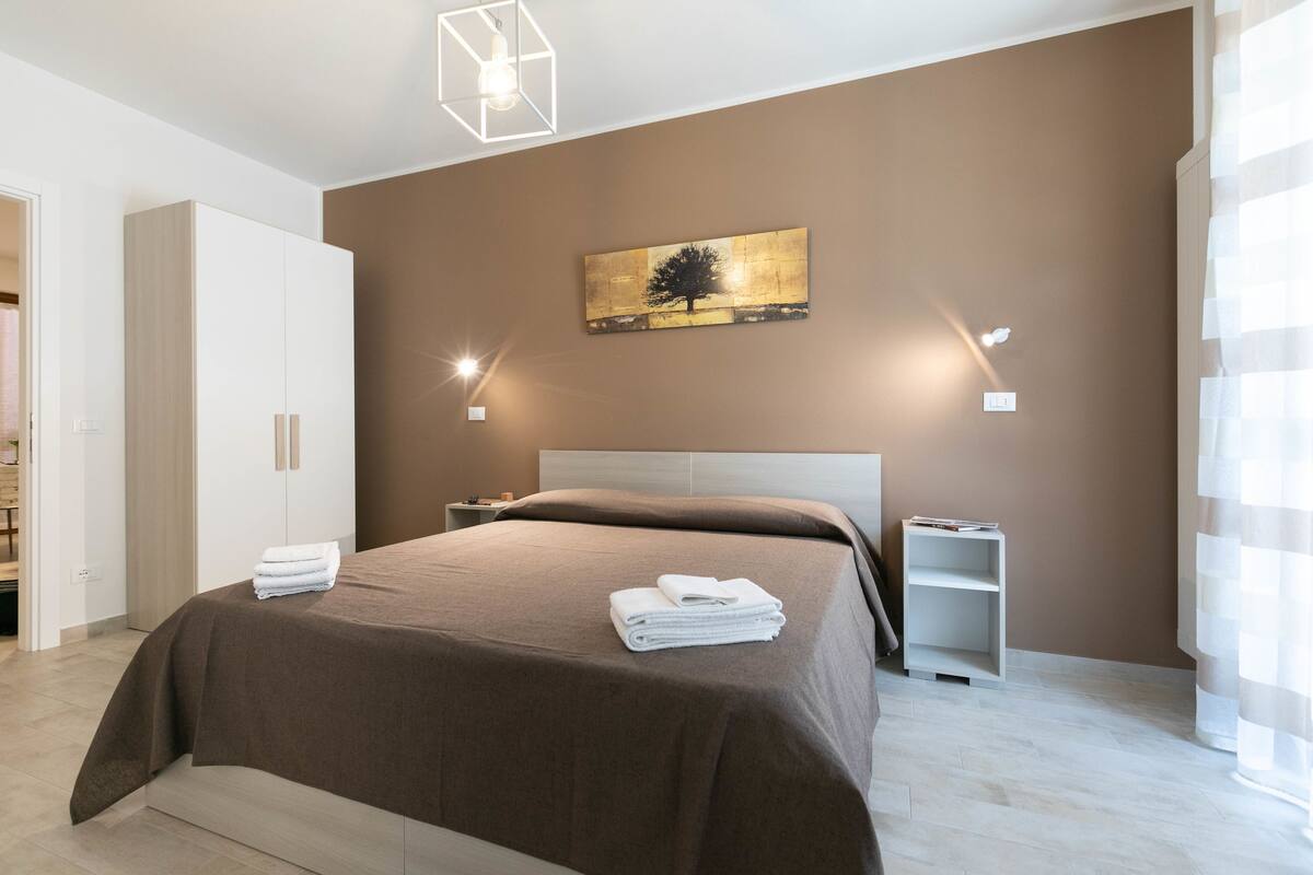 Un dormitorio moderno con una cama grande, una mesita de noche, una lámpara de pared y un cuadro.
