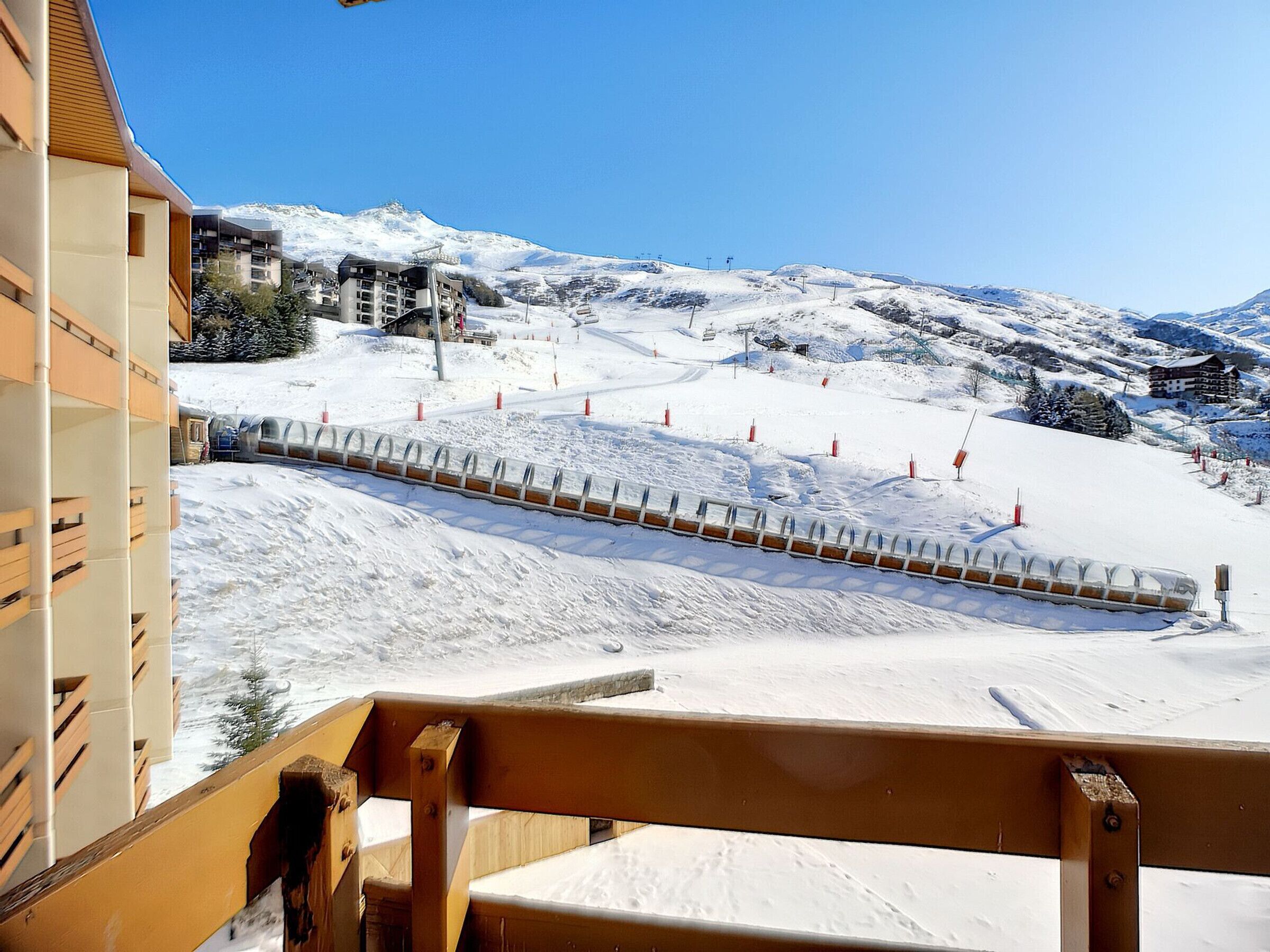 A snow-covered ski slope with a wooden barrier and a building in the foreground.