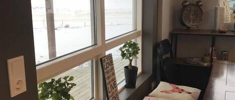 A room with a large window, a small table with a chair, a potted plant, and a decorative sign.