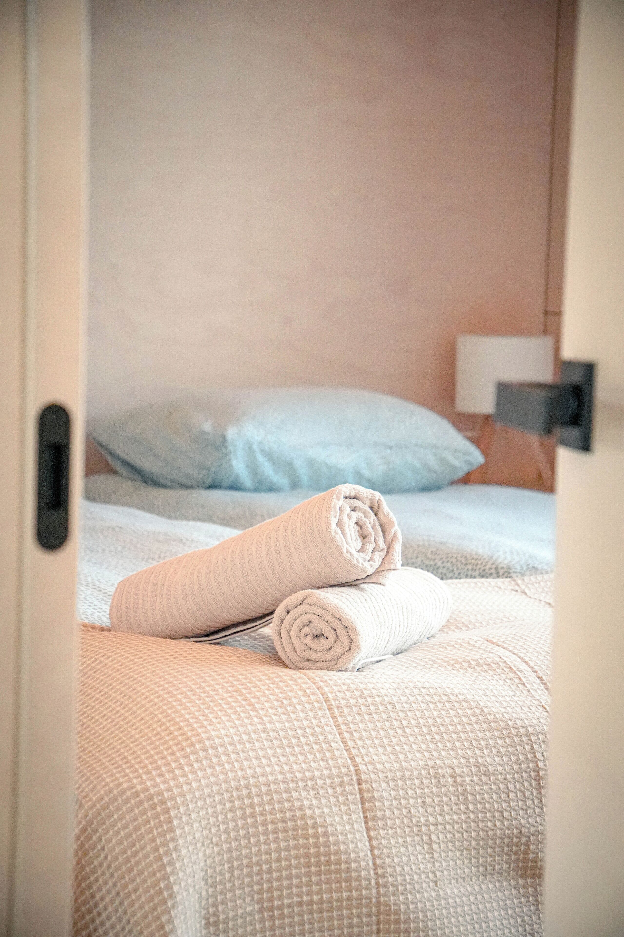 A hotel room with a bed, a rolled towel, and a nightstand with a lamp.