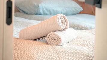 A hotel room with a bed, a rolled towel, and a nightstand with a lamp.
