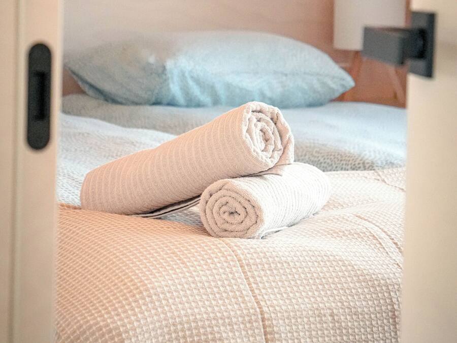 A hotel room with a bed, a rolled towel, and a nightstand with a lamp.