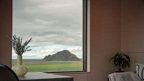A room with a view of a landscape through a large window, a table with a vase, and a plant on a side table. - Stóra Mörk Guesthouse (Rangárþing eystra)