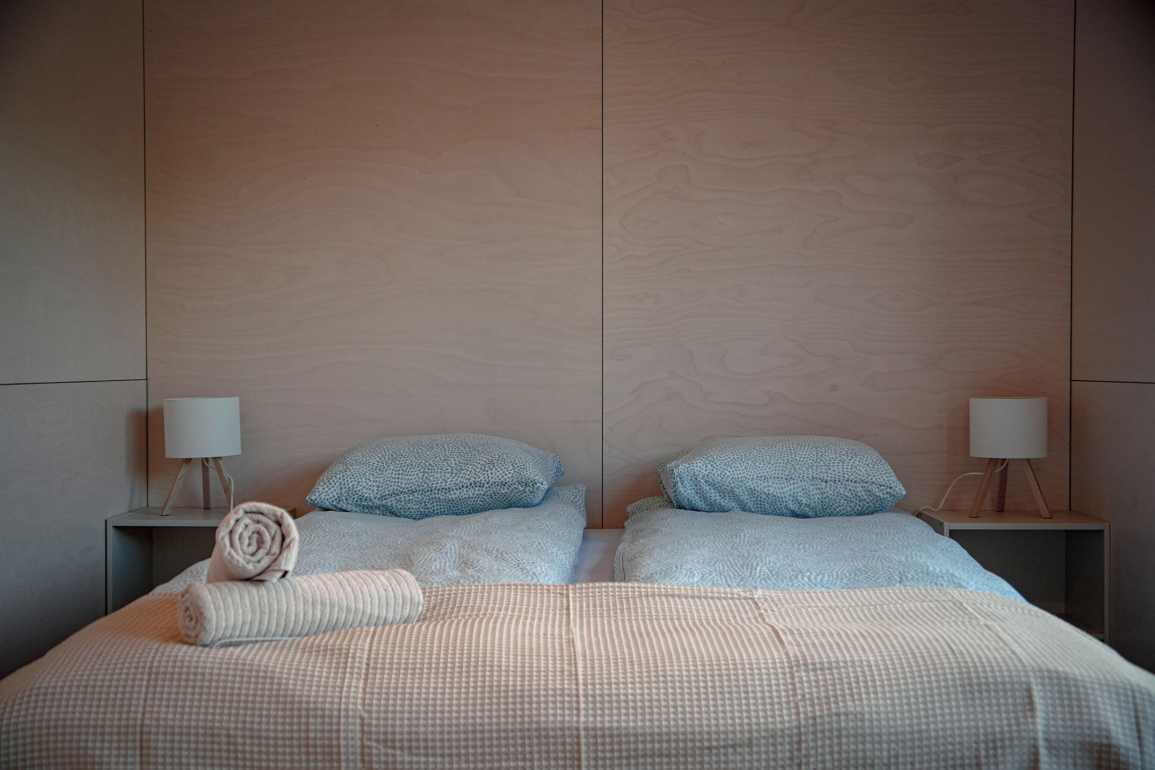 A double bed with a checkered bedspread, two pillows, and a rolled towel. There are two bedside tables with lamps.