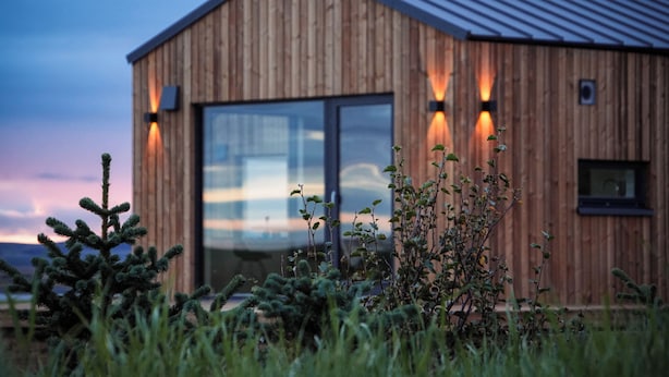 A modern wooden building with large windows and exterior lighting. - Stóra Mörk Guesthouse (Rangárþing eystra)