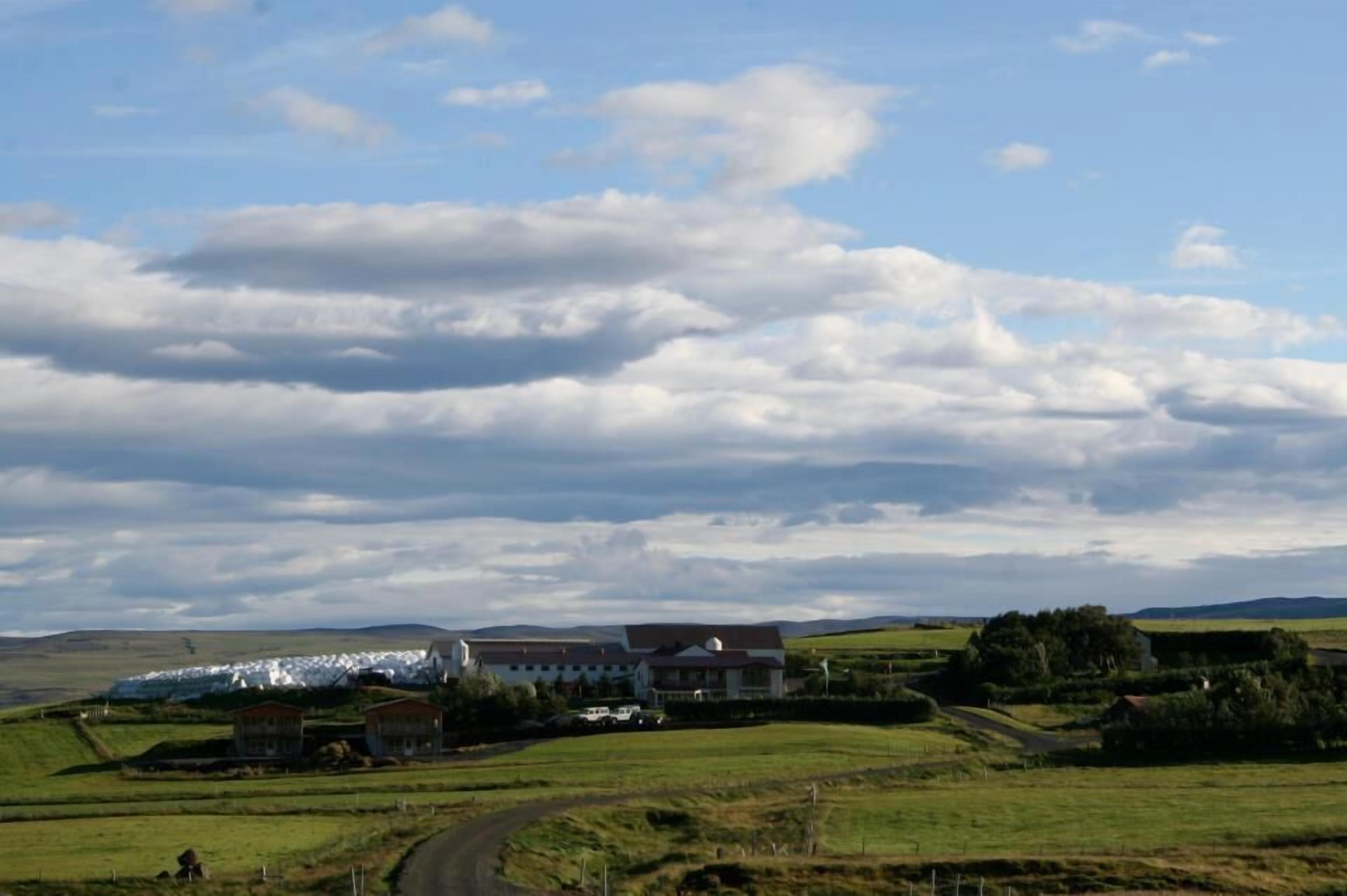 A rural landscape with a large white building, possibly a hotel, surrounded by green fields and a winding road.