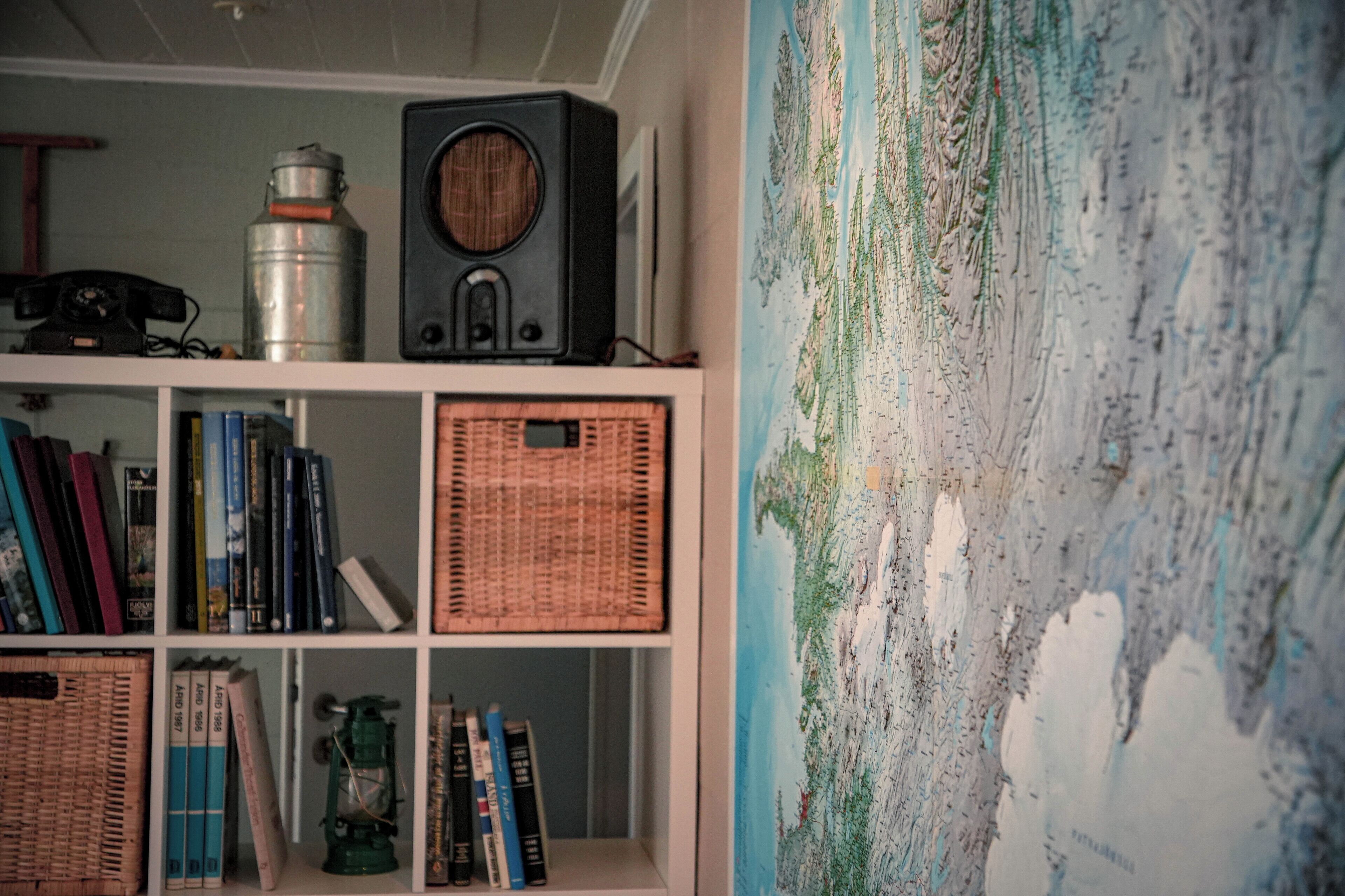 Une bibliothèque remplie de livres et une vieille radio, une carte du monde accrochée au mur et un récipient en métal.