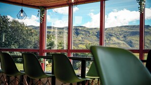 A room with large windows offering a view of a mountainous landscape. There are several green chairs arranged in front of the windows. - Stóra Mörk Guesthouse (Rangárþing eystra)