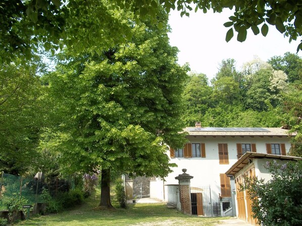 A white building with a tiled roof, surrounded by lush greenery and trees. - Affittacamere Il Tiglio (Cavagnolo)