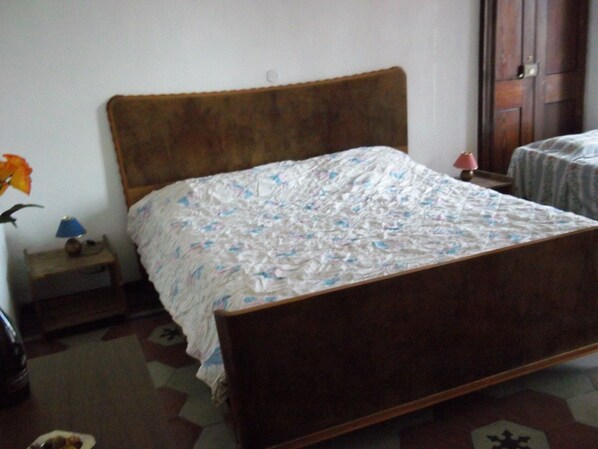 Un dormitorio con una cama de madera, una mesita de noche con lámpara y una pequeña mesa con un florero.