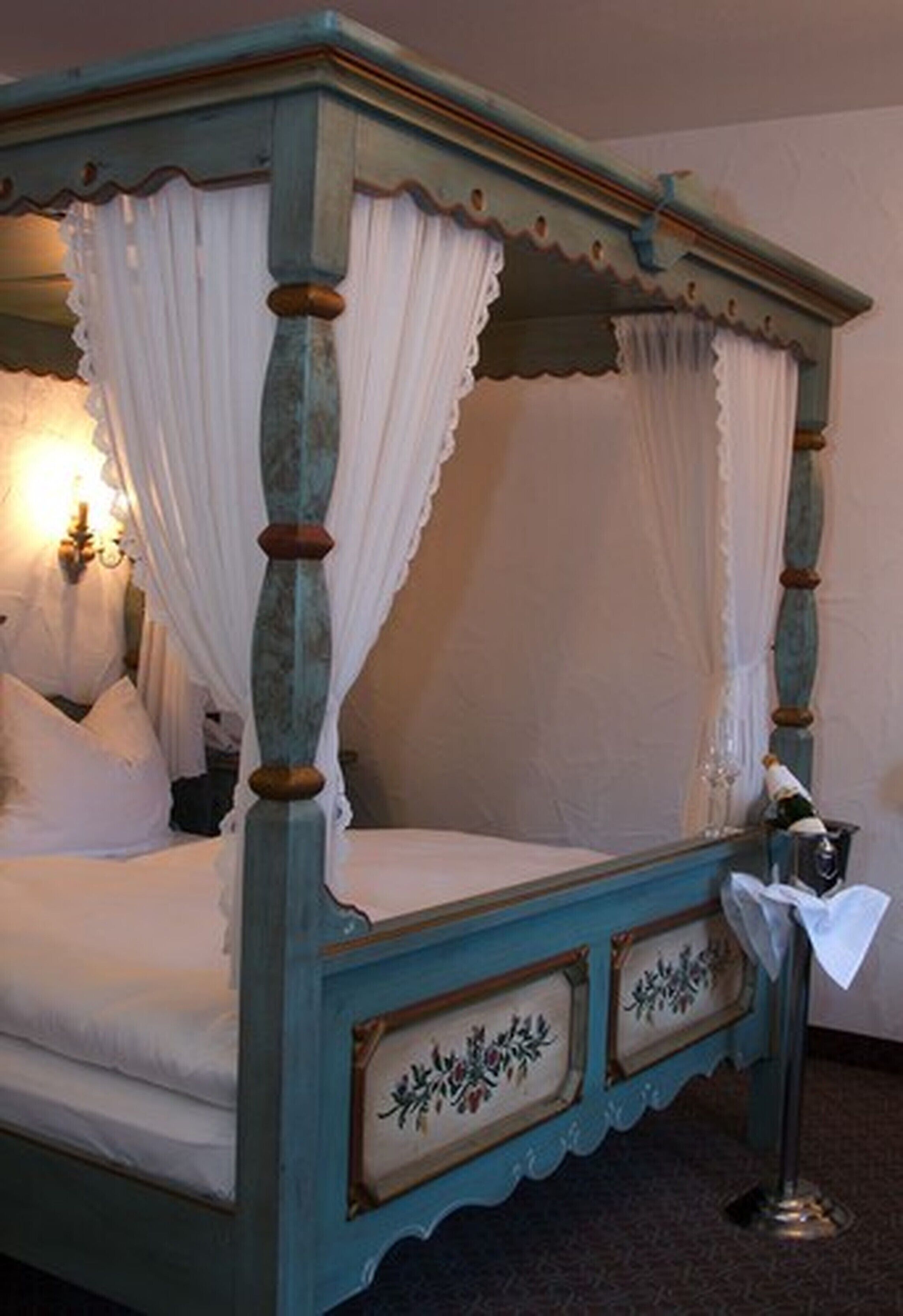 A four-poster bed with a canopy, a bedside table with a lamp, and a framed picture on the headboard.
