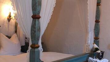 A four-poster bed with a canopy, a bedside table with a lamp, and a framed picture on the headboard.
