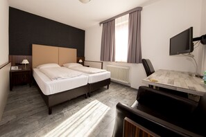 Habitación de hotel con cama doble, escritorio con silla, televisión y ventana con cortinas.