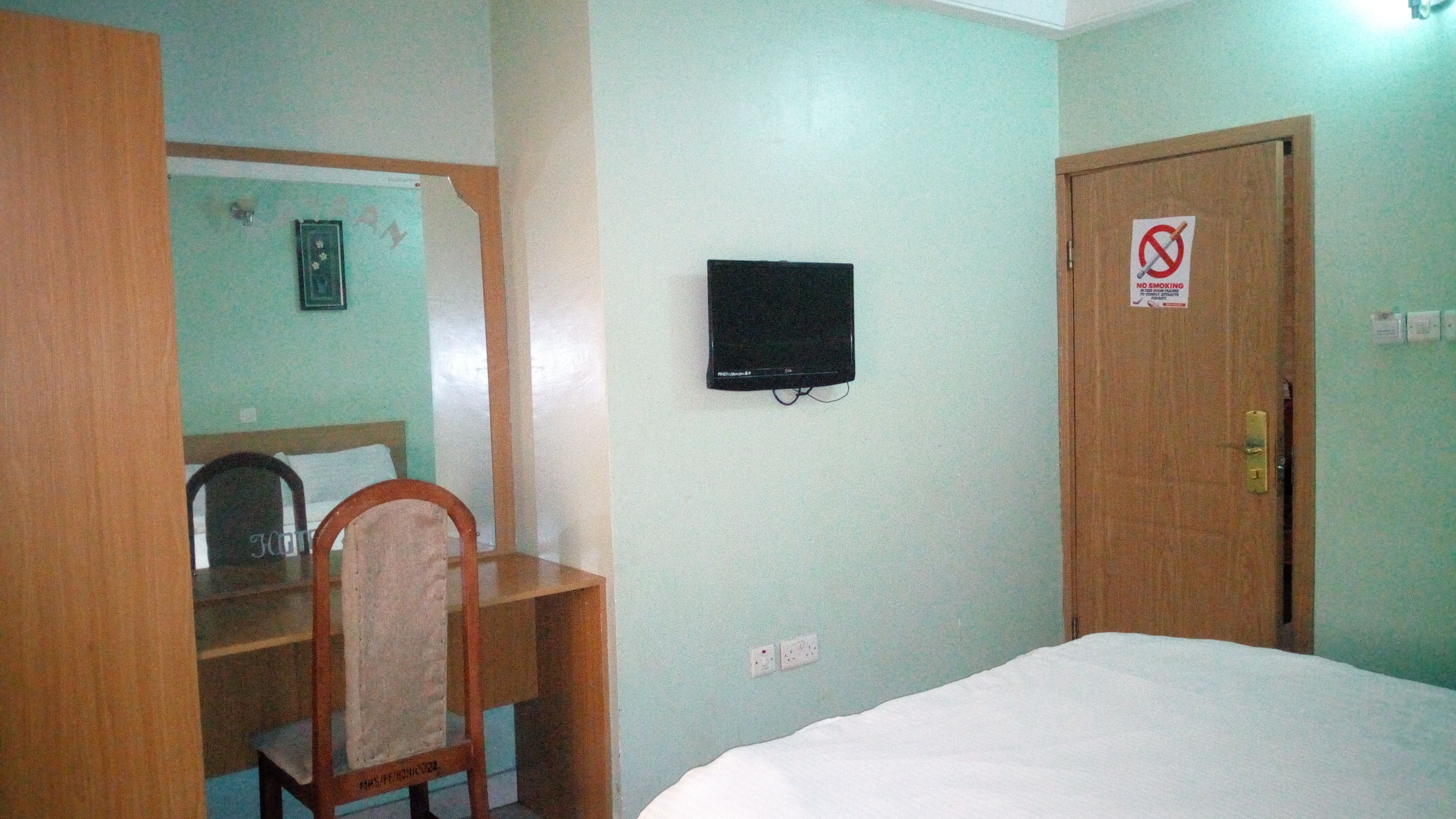 A room with a bed, a desk, a chair, a television, and a door with a 'No Smoking' sign.