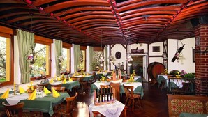 Un restaurant avec des tables et des chaises en bois, des nappes vertes et un mur en briques.