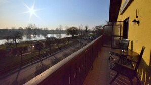 Un balcon donnant sur un lac, une table avec des chaises et un mur jaune orné d’une horloge.