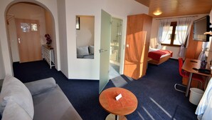 Une chambre d’hôtel de taille réduite, comprenant un canapé, une petite table, un lit, une télévision et un espace douche.