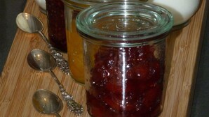 Four glass jars with lids on a wooden surface, accompanied by two metal spoons. - Chambres d'hôtes Au BO Voyage (Tavant)