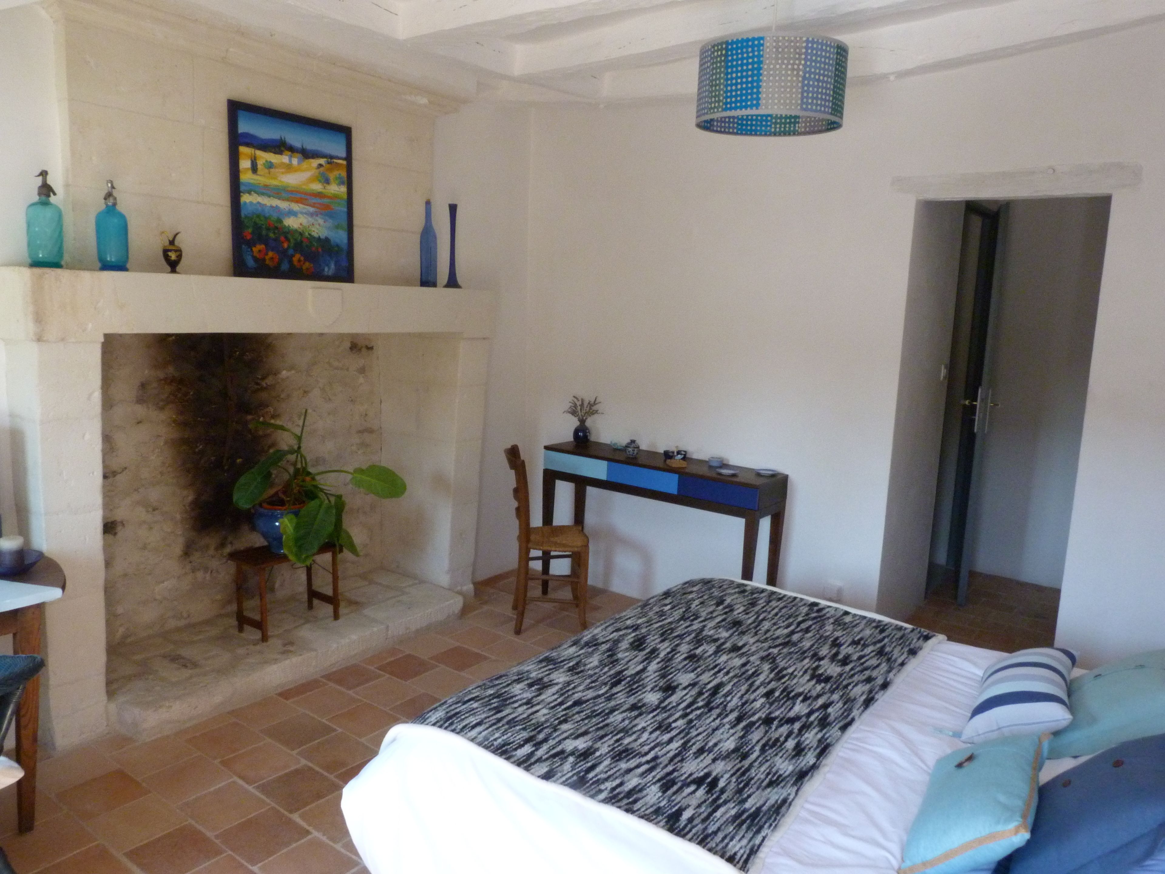 A bedroom with a bed, a desk, a chair, a fireplace, and a door.
