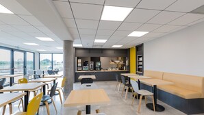 Un moderno comedor con mesas y sillas, una barra con caja registradora y vistas amplias a través de grandes ventanales.