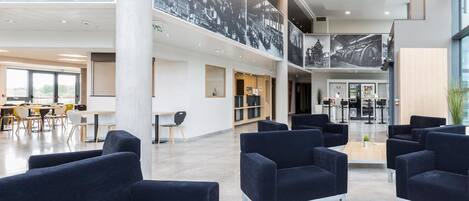 A spacious lobby with modern black sofas, a wooden coffee table, and large black-and-white photographs on the walls.