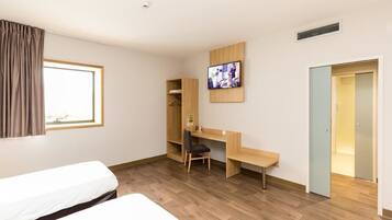 A hotel room with a bed, a desk with a chair, a television, and a wardrobe.