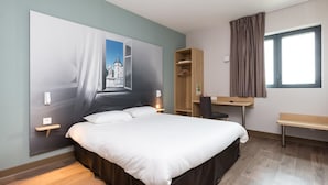 Habitación de hotel moderna con una cama grande, un escritorio, un armario y vistas a un castillo a través de una ventana abierta.