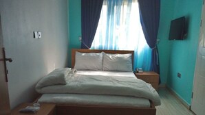 A bedroom with a bed, nightstands, a wooden bench, a TV on the wall, and a window with curtains. - Graceville Comfort Residence (Abuja)