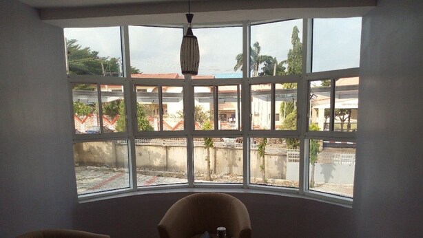 A room with a curved window, a desk with a laptop, two chairs, and a hanging light fixture. - Graceville Comfort Residence (Abuja)