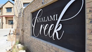 Un letrero con el nombre 'Kyalami Creek' en una fuente cursiva sobre un fondo oscuro, colocado en una pared de ladrillo.