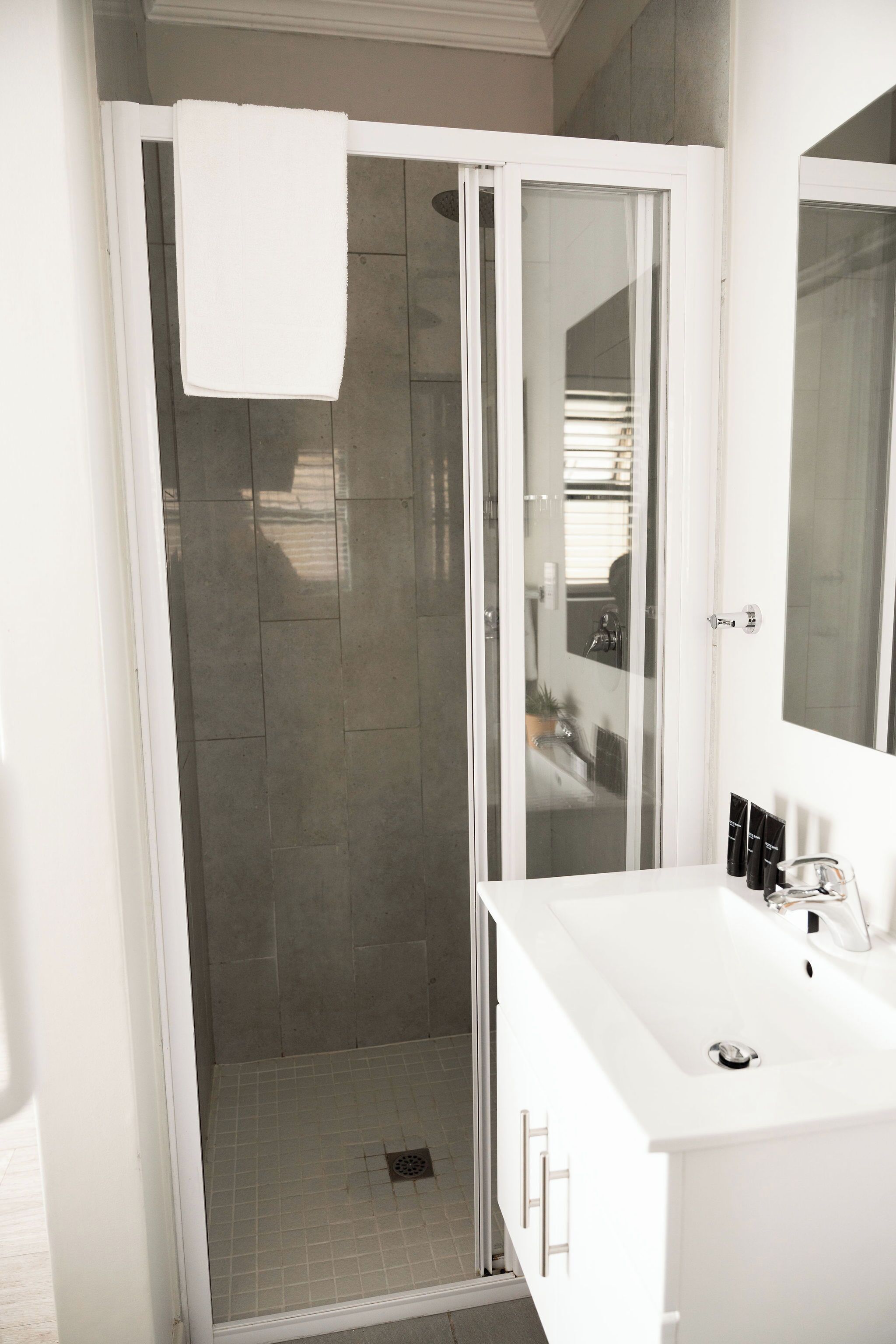 A modern bathroom with a glass-enclosed shower, a white sink, and a large mirror.