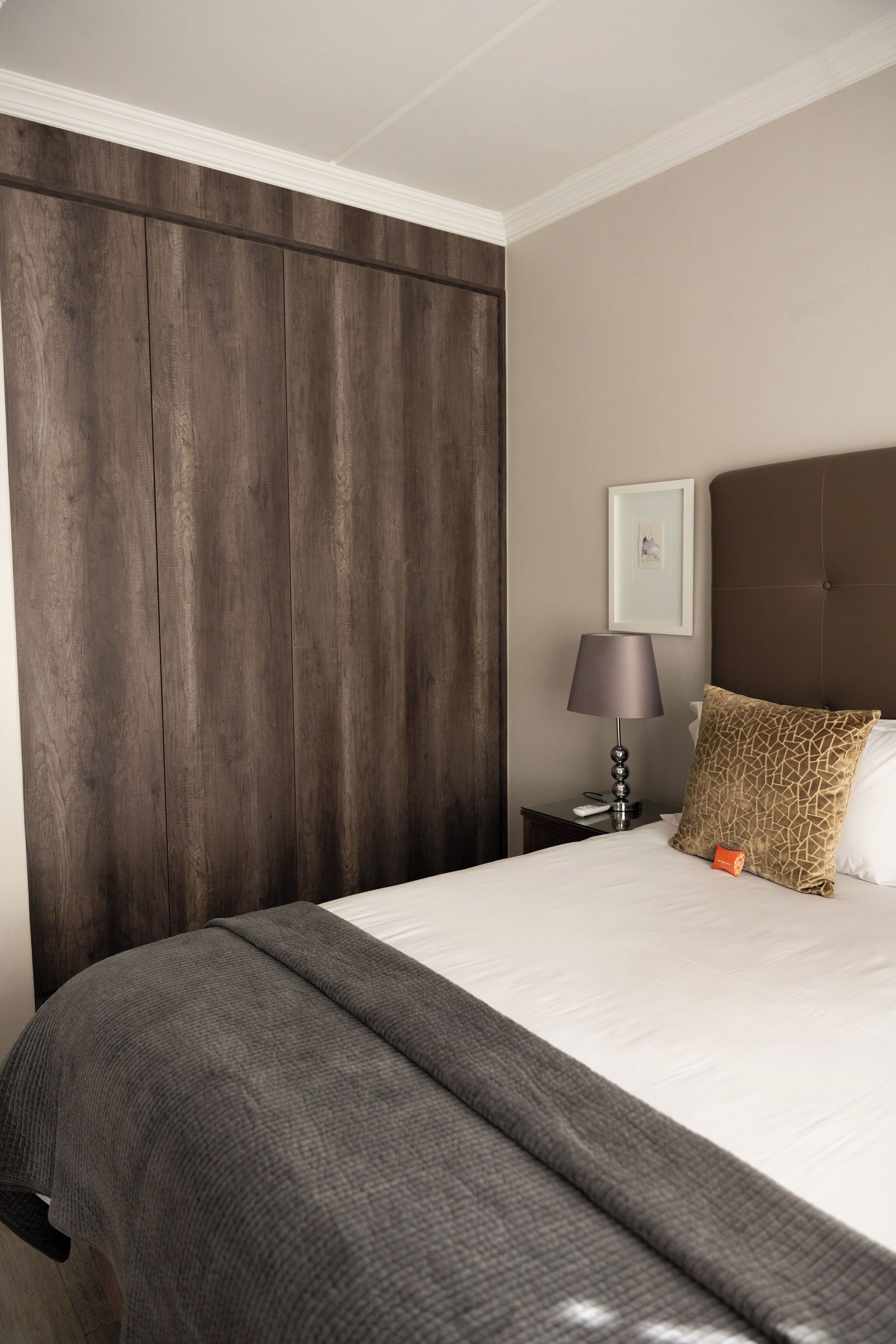 Ein Hotelzimmer mit einem großen Bett, einem Holzkopfende, einem Nachttisch mit Lampe und einem gerahmten Bild an der Wand.
