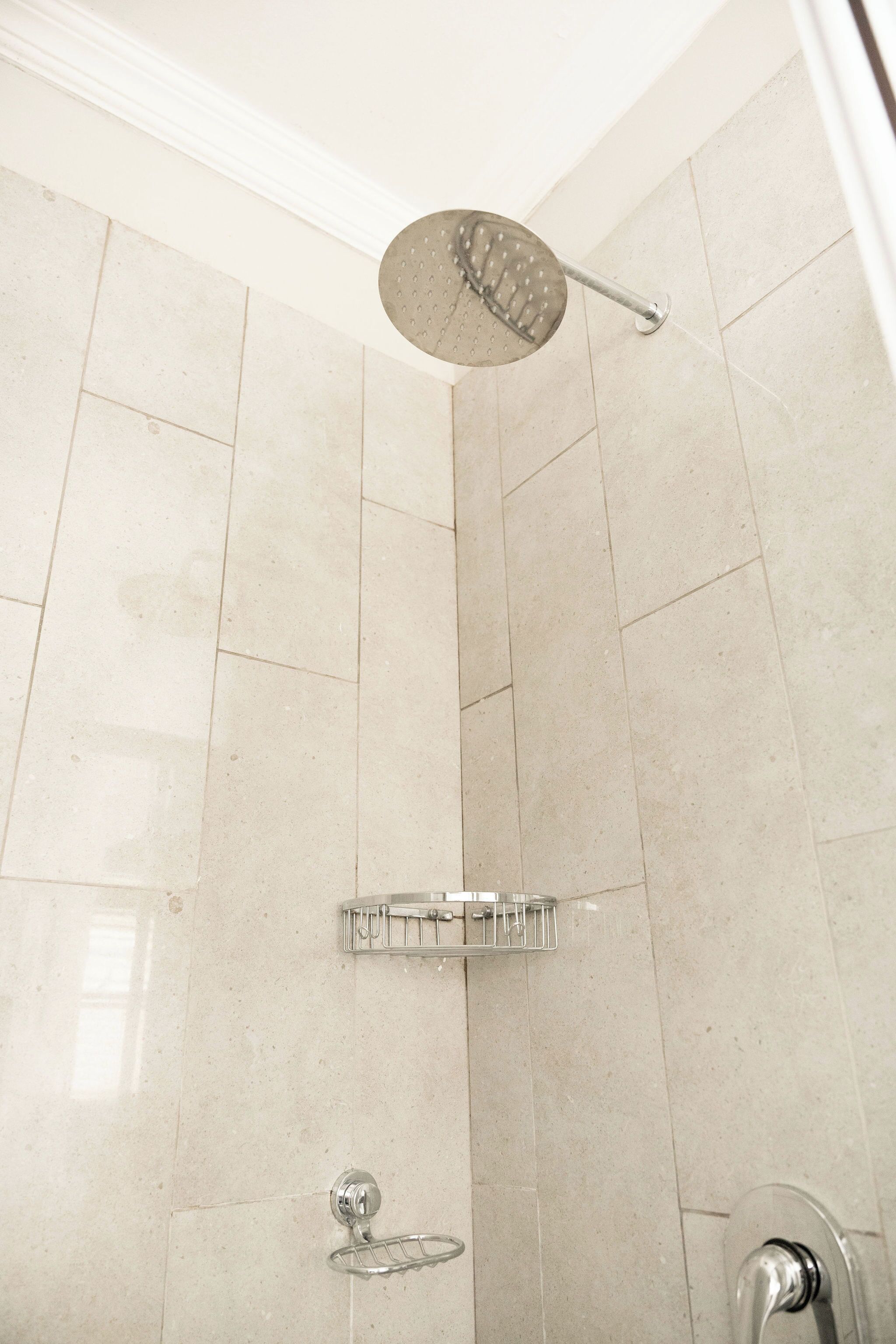 A shower with a handheld showerhead, a glass shelf, and a wall-mounted faucet.
