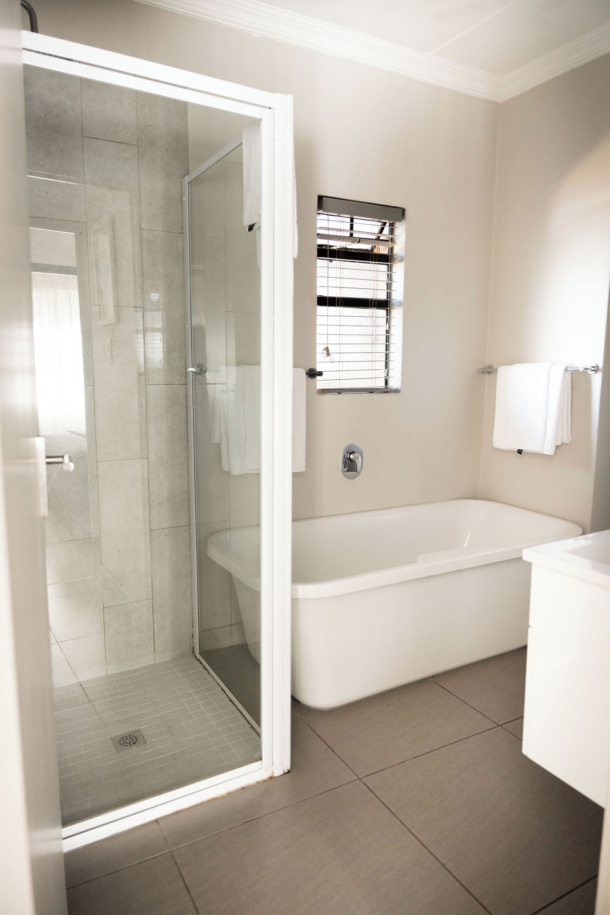 A modern bathroom with a glass-enclosed shower, a freestanding bathtub, and a small window above the sink.