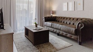 Una sala de estar moderna con un sofá de cuero, una mesa de centro de madera, un televisor y un amplio ventanal con cortinas.