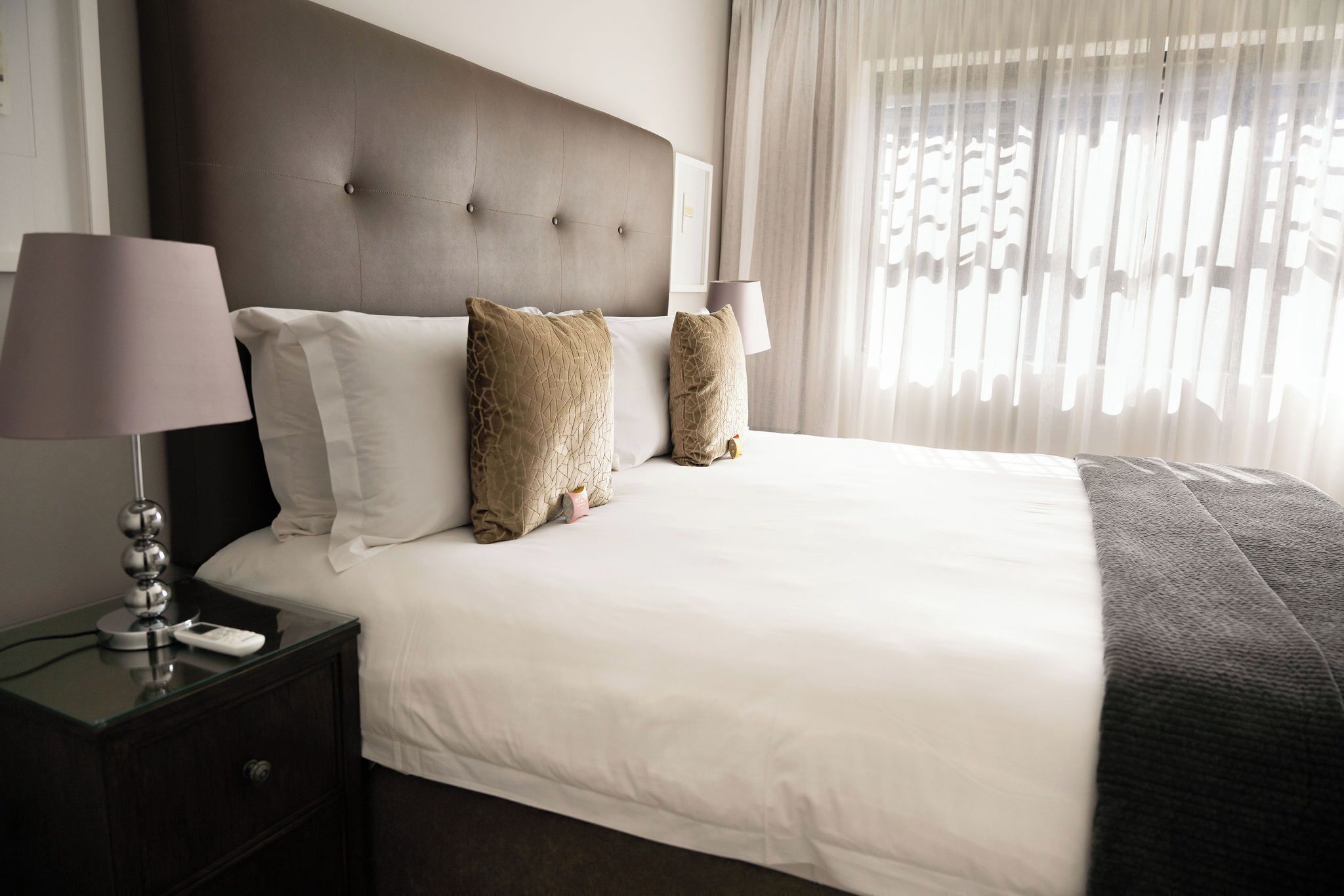 A neatly made bed with a dark headboard, two bedside lamps, and a nightstand with a lamp and a phone.