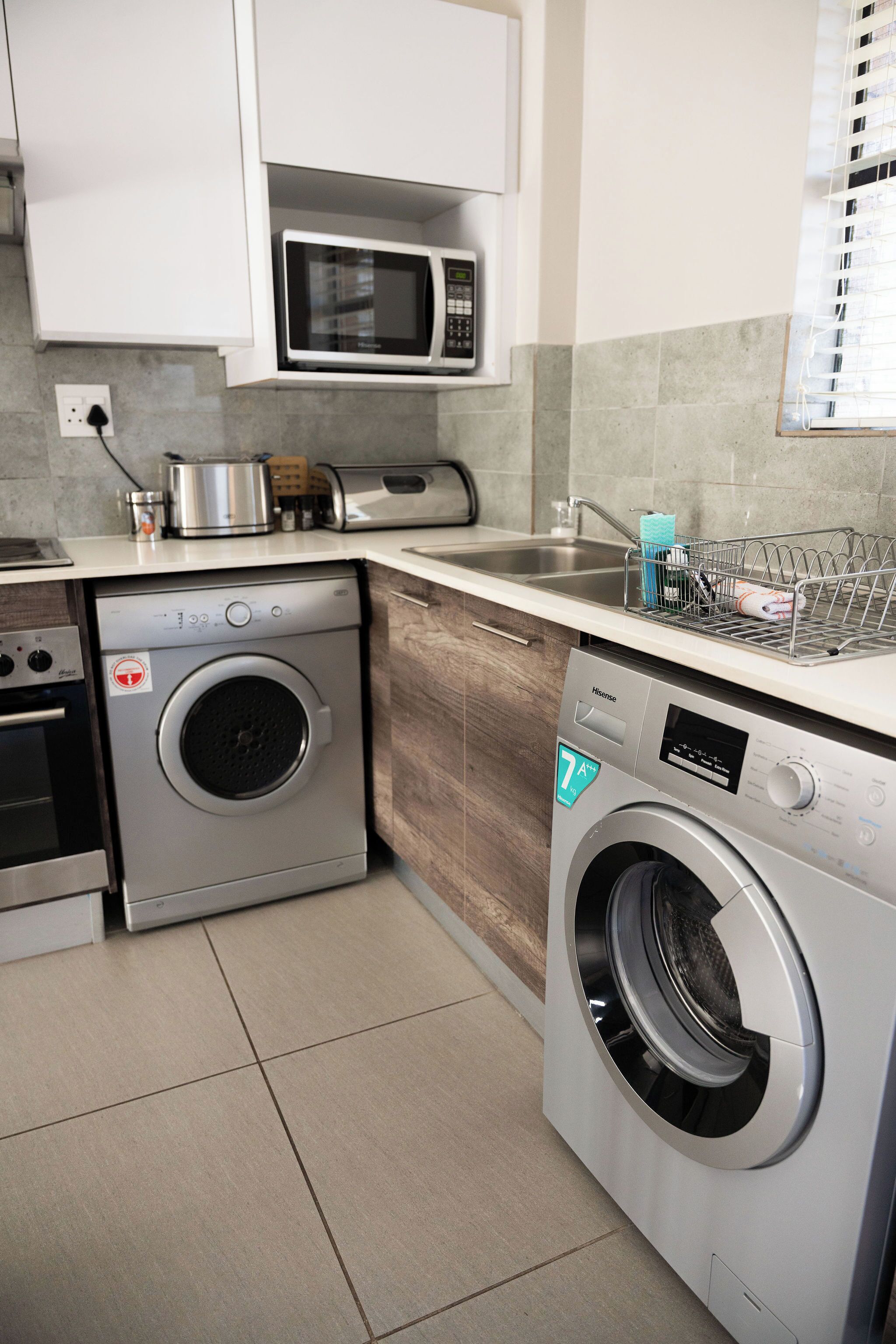 Une cuisine compacte équipée d’un lave-linge, d’un four à micro-ondes et d’un égouttoir à vaisselle posé sur le plan de travail.