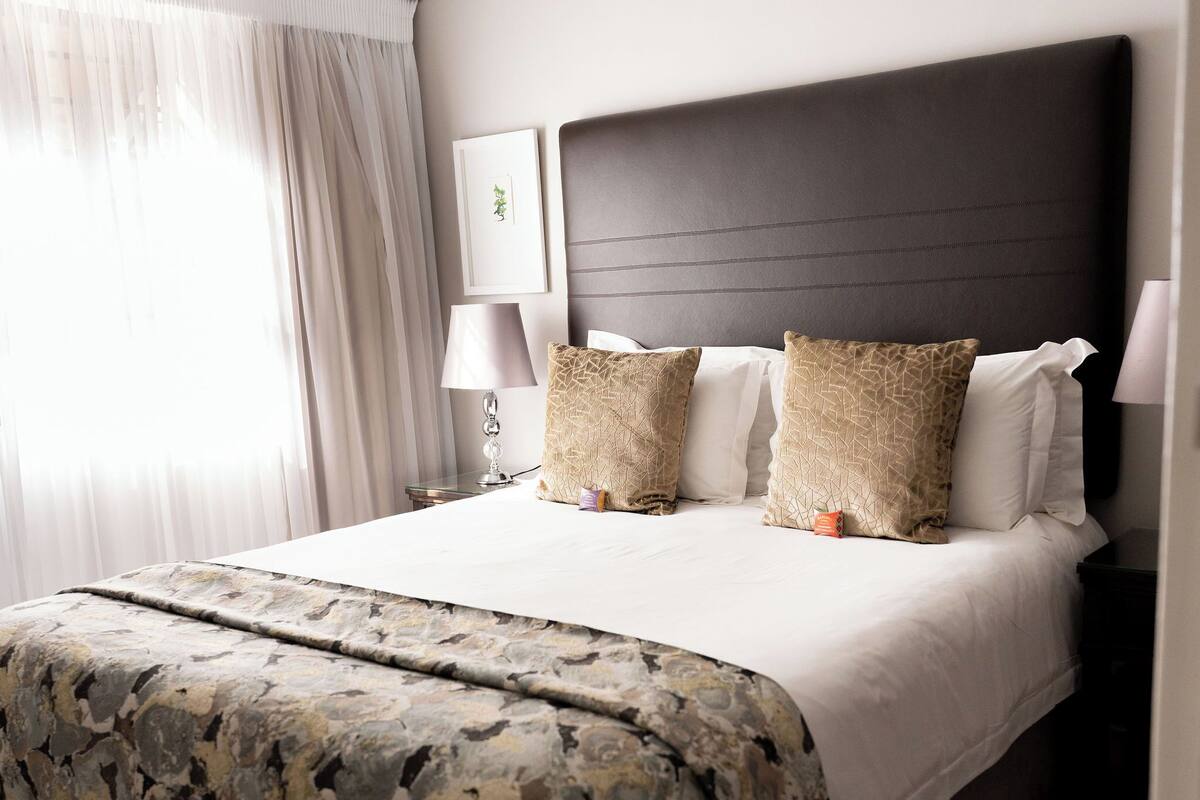 A neatly made bed with a patterned bedspread, a dark headboard, and two bedside lamps.
