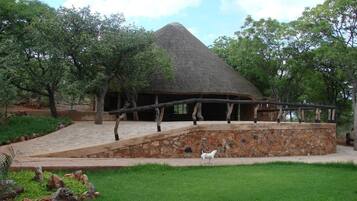 Situated in a lush landscape, this charming building features a thatched roof and a stone wall, with a wooden bridge connecting it to the surrounding environment.